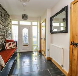 An entrance hallway with a stone wall bench with red cushions a wooden door a radiator and a wall mirror at Mynydd ar Mor in Barmouth