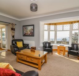 A living room with leather chairs and a wooden coffee table near a bay window with a sea view at Mynydd ar Mor in Barmouth