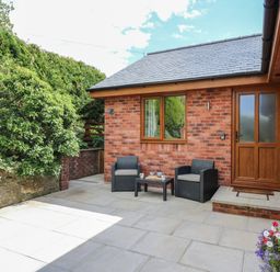 A patio area with two chairs and a table outside a brick house at Awel y Bryn in Rhayader