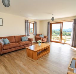 A living room with brown sofas coffee table and large glass doors with a view at Awel y Bryn in Rhayader