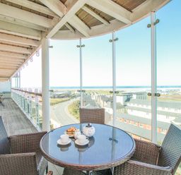 A balcony with a round glass table and four wicker chairs overlooking buildings and a road at Sunset View in Castletown Portland