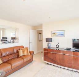 A living room with a brown leather sofa cushions a wall mirror a wooden cabinet with a TV lamp and decorative items at Sunset View in Castletown Portland