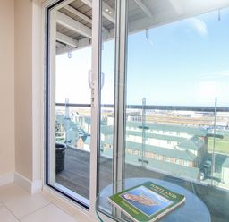 A glass door opening to a balcony with a view of buildings and a book on a round glass table at Sunset View in Castletown Portland