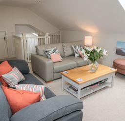 A sitting area with sofas a coffee table flowers and an ottoman at The Coach House in Bamburgh