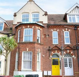 A row of brick townhouses with white framed windows and doors with one door painted yellow with a tree and bins in front at Flat 3 in Cromer