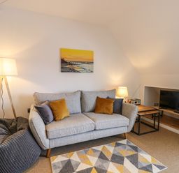 A living room with a grey sofa with pillows a patterned rug a bean bag floor lamp and a TV on a shelf at Flat 3 in Cromer