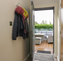 A hallway with coats hanging on hooks and a door open to a deck with outdoor seating at Bay Tree Lodge in Cartmel
