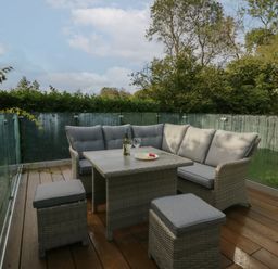 An outdoor patio with grey cushioned seating a table with a bottle and glasses surrounded by glass railing at Bay Tree Lodge in Cartmel
