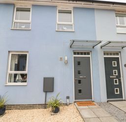 The front of a blue house with two doors and four windows with plants in pots and welcome mat on one door at Ty Glas in Ogmore-by-Sea near St Brides Major