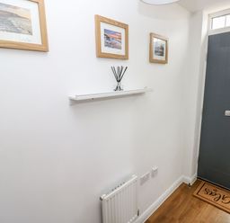 An entryway with a dark gray door a white wall with three framed pictures a small shelf with a reed diffuser a radiator and a doormat at Ty Glas in Ogmore-by-Sea near St Brides Major