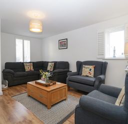 A living room with blue sofas a wooden coffee table and a lamp at Ty Glas in Ogmore-by-Sea near St Brides Major