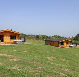 Two wooden lodges on a grassy area with outdoor seating and hot tubs at Foxglove Lodge in Hittisleigh