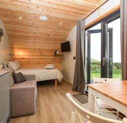 A wooden cabin interior with a bed sofa kitchen area dining table and glass doors leading outside at Orchard in Dalton-In-Furness