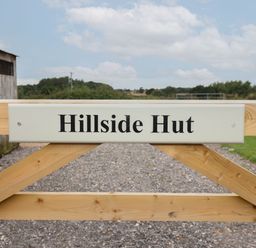 A wooden gate with a sign that reads Hillside Hut on a gravel path in a rural area at Hillside Hut in Radbourne near Ashbourne