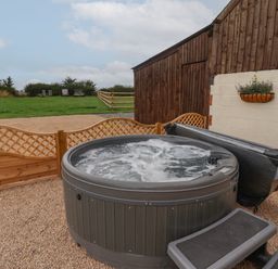 An outdoor hot tub with water bubbling next to a wooden fence and a wooden building at Hillside Hut in Radbourne near Ashbourne
