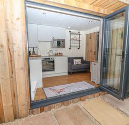 A small kitchen living area with white cabinets gray sofa and glass folding door at Hillside Hut in Radbourne near Ashbourne