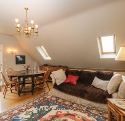 A living room with a sofa cushions a wooden dining table four chairs and a patterned rug at The Barn at Westhall Cottage Fulbrook near Burford