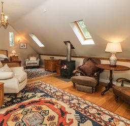 An attic bedroom with armchairs a bed a wood burning stove and skylight windows at The Barn at Westhall Cottage in Fulbrook near Burford