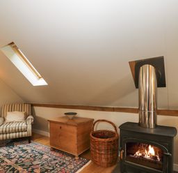A room with a striped armchair wooden chest woven basket lit fireplace and skylight window at The Barn at Westhall Cottage Fulbrook near Burford
