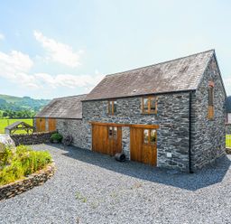 A stone house with wooden doors and a gravel driveway at The Barn in Corwen