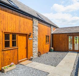 An outdoor view of a wooden structure with a stone wall and pathway at The Barn in Corwen