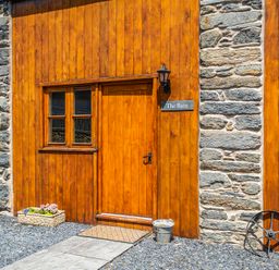 A rustic entrance with wooden door and stone wall at The Barn in Corwen