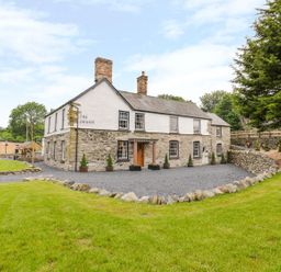 A stone and white exterior house with chimneys surrounded by grass and stone walls at The Druids in Druid near Corwen