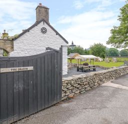 A black wooden gate with the sign The Druids stone wall and white building with chimney near a garden with seating and trees at The Druids in Druid near Corwen