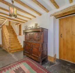 A hallway with wooden stairs wooden doors a wooden cabinet a decorative light and a rug at The Druids in Druid near Corwen