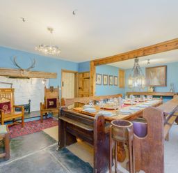 A dining room with a wooden dining table set with plates and glasses and wooden chairs at The Druids in Druid near Corwen