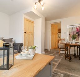 A living room with a wooden table, sofa, two doors, and dining area with chairs at The Wonky Burrow in Bowness-On-Windermere