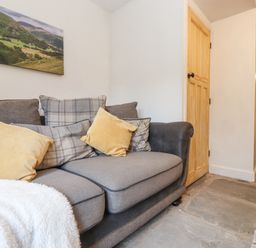 A grey sofa with yellow and plaid cushions and a white throw in a room with wooden doors and stone flooring at The Wonky Burrow in Bowness-On-Windermere