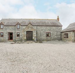 A stone house with several windows doors and a gravel driveway at Caerdegog Ganol Cemlyn near Cemaes Bay