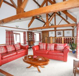 A living room with red leather sofas and wooden beams at Caerdegog Ganol in Cemlyn near Cemaes Bay