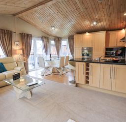 An open living room and kitchen with beige sofas glass dining table and wooden ceiling at Our Happy Place Lakeside 16 Borwick near Carnforth