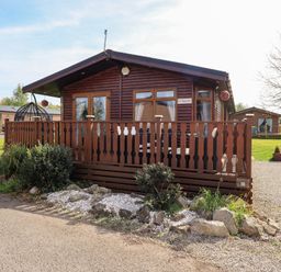 A wooden cabin with a fenced porch and plants in front at Our Happy Place Lakeside 16 Borwick near Carnforth
