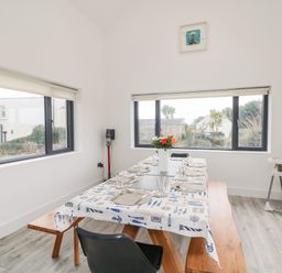 A dining room with a table set for eight people a vase with flowers on the table a high chair in the corner and large windows at Old Field House Slade near Fethard-On-Sea County Wexford
