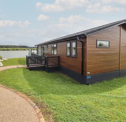 A brown wooden cabin with black trim on a grassy area near a lake at 40 Delamere Point in Delamere