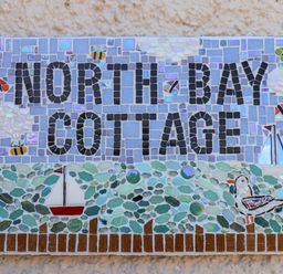 A mosaic sign with text north bay cottage decorated with sailboats birds and bees at North Bay Cottage in Bridlington