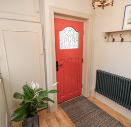 An entryway with a red door a plant on the left a black radiator on the right and a wall-mounted coat rack at North Bay Cottage in Bridlington