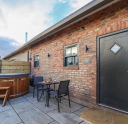 An outdoor patio with a black door, two windows, a wood hot tub, and a small table with two chairs at Robins Nest in Pocklington