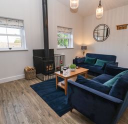 A living room with two blue sofas a wooden coffee table a wood stove and two windows at Robins Nest in Pocklington