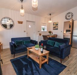 A living room with two blue sofas around a wooden coffee table with wine glasses and a bottle at Robins Nest in Pocklington