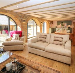 A living room and kitchen with beige sofas a wooden dining table and stone wall arches at The Coach House in Great Whittington near Corbridge