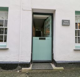 The exterior of a building with a half-open mint green door and two windows with white frames at Aunt Dora's in Port Isaac