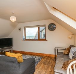 A living room with two sofas a television a wall clock and a window with a sea view at Old Field Hideaway Slade near Fethard-On-Sea County Wexford