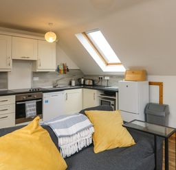 A kitchen with white cabinets and appliances and a gray couch with yellow pillows at Old Field Hideaway Slade near Fethard-On-Sea County Wexford