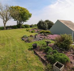 A garden with trimmed grass trees bushes and a small building at Tower Cottage Near Pembroke