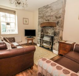 A living room with brown leather sofas a stone fireplace a small wooden table with a television and a window at Ty Potiwr Conwy