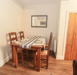 A dining area with a wooden table and four chairs a table runner and placemats on the table a mirror on the wall and a wooden door to the side at Ty Potiwr in Conwy